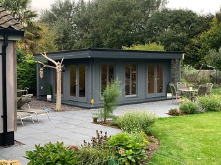 Modern grey shed with large windows on patio surrounded by garden and trees